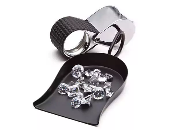 A selection of diamonds on a tray, next to a jewellers magnifying glass.