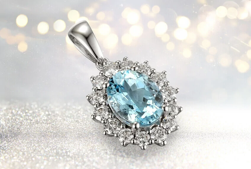 Aquamarine and diamond pendant, with a sparkly base and dim lights in the background. The birthstone for March.